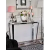 Konsola glamour Ralph w nowoczesnym salonie, udekorowana książkami, lampą i świecami, stoi obok czarnej sofy.