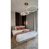 Nowoczesny żyrandol Crystal XXL z trzema ringami podwieszony nad łóżkiem w jasnej sypialni z szarymi zasłonami.