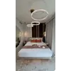 Potrójny żyrandol Crystal XXL w złocie nad łóżkiem w eleganckiej sypialni z jasnymi zasłonami i ciemną ścianą.