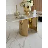 Ujęcie z boku stołu glamour ROKSI w jasnym wnętrzu, pokazujące jego strzeliste złote nogi marmurowe, w ofercie Primavera Home.