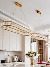 Dwa żyrandole nowoczesne złote Crystal zawieszone nad wyspą kuchenną w jasnej, eleganckiej kuchni.
