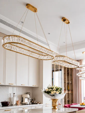Dwa żyrandole nowoczesne złote Crystal zawieszone nad wyspą kuchenną w jasnej, eleganckiej kuchni.