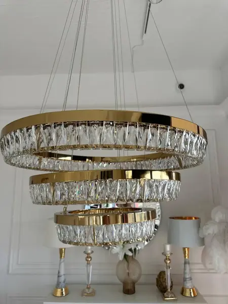 Perspektywiczne ujęcie żyrandola kryształowego złotego BELLINI XL w eleganckim wnętrzu. Lampa od Primavera Home.
