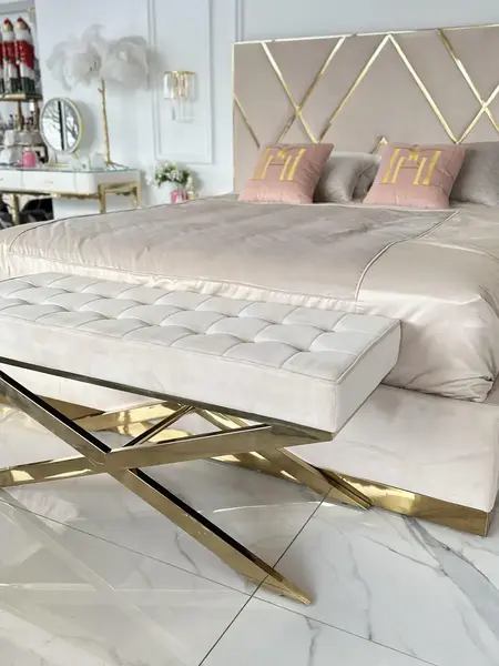 Zbliżenie na złote krzyżakowe nóżki pufy, podkreślające jej elegancję. Propozycja od Primavera Home.