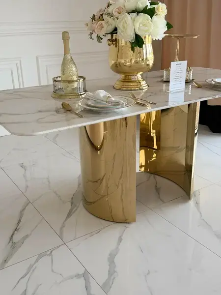 Ujęcie z boku stołu glamour ROKSI w jasnym wnętrzu, pokazujące jego strzeliste złote nogi marmurowe, w ofercie Primavera Home.
