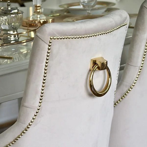 Ekskluzywne krzesło do jadalni, pikowane, z kołatką, glamour, nowojorskie, drewniany stelaż, nowoczesne, złote PRINCE umieszczone przy stole. Elegancja od Primavera Home.