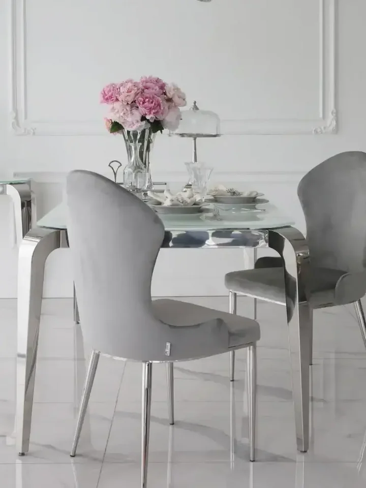 Szeroki widok z daleka na designerski stół glamour ze szklanym blatem, stalowy, nowoczesny, srebrny ELITE, prezentujący się efektownie w przestrzeni od Primavera Home.