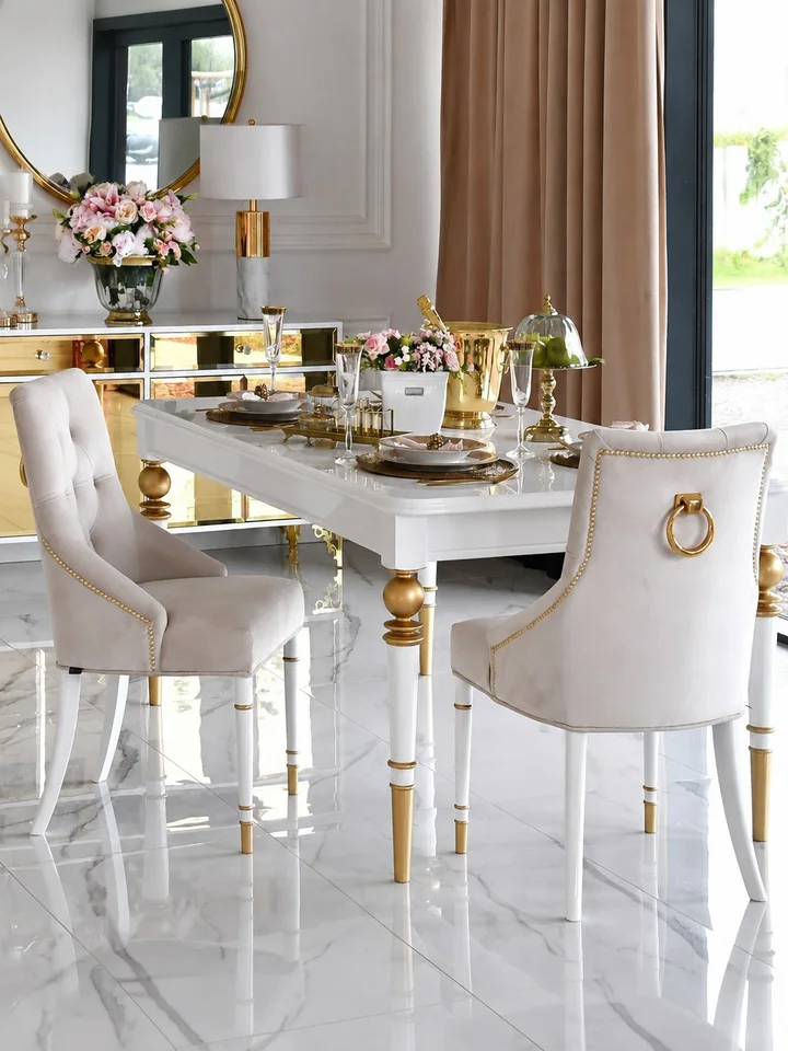 Stół Queen glamour z białym blatem i złotymi detalami w eleganckiej jadalni Primavera Home, otoczony jasnymi krzesłami i dekoracjami kwiatowymi.