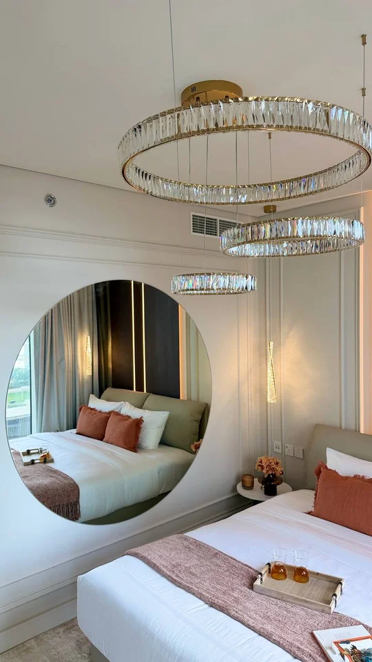Żyrandol Crystal XXL odbijający się w dużym, okrągłym lustrze w eleganckiej sypialni.