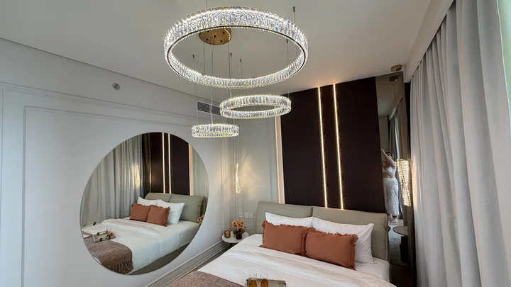 Trzy ringi żyrandola Crystal XXL w złotej oprawie nad łóżkiem z podświetlaną ramą i zasłonami.