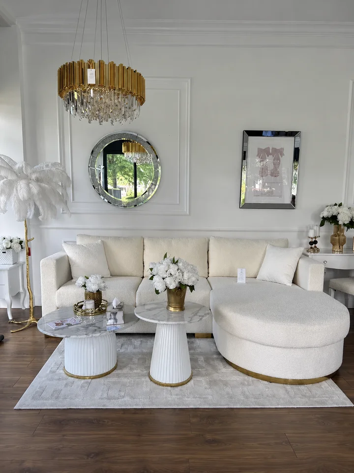 Dwa białe stoliki Kendall ustawione na jasnym dywanie, przed kremową sofą i dużą pufą w eleganckim salonie.