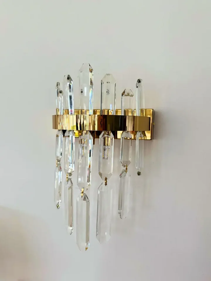 Kinkiet kryształowy, złoty, glamour, designerska lampa ścienna BULGARI umieszczony obok sofy. Meble na zamówienie od Primavera Home.