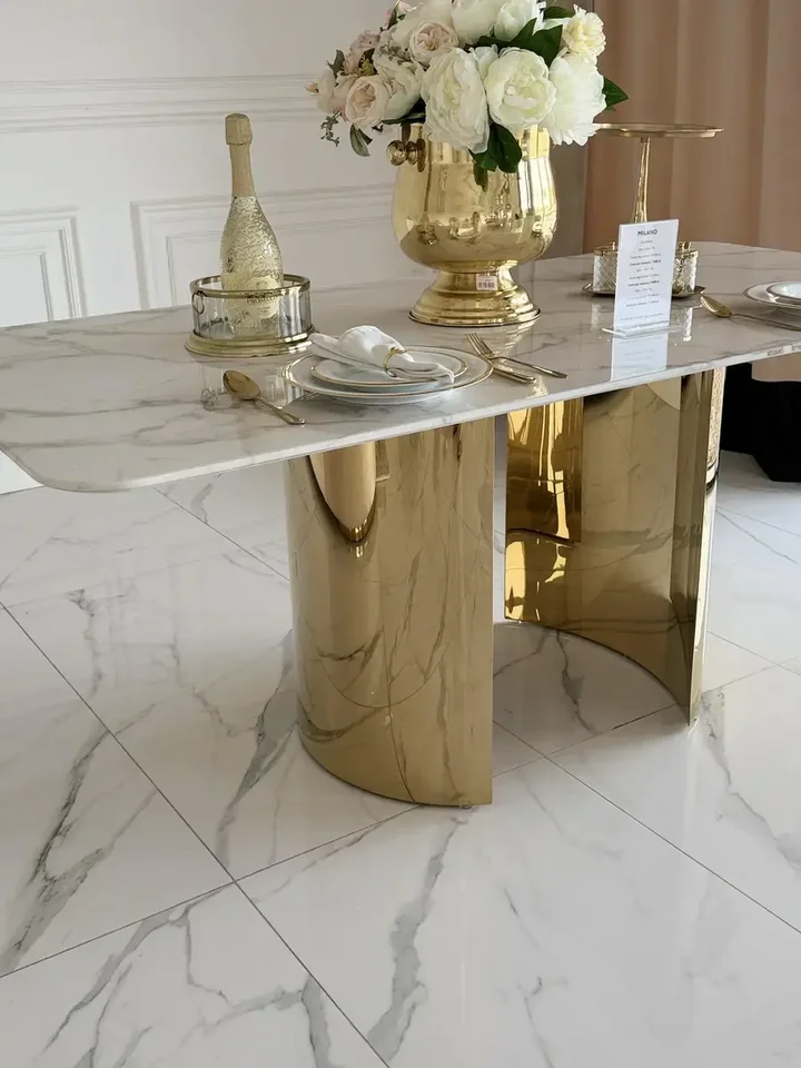 Ujęcie z boku stołu glamour ROKSI w jasnym wnętrzu, pokazujące jego strzeliste złote nogi marmurowe, w ofercie Primavera Home.
